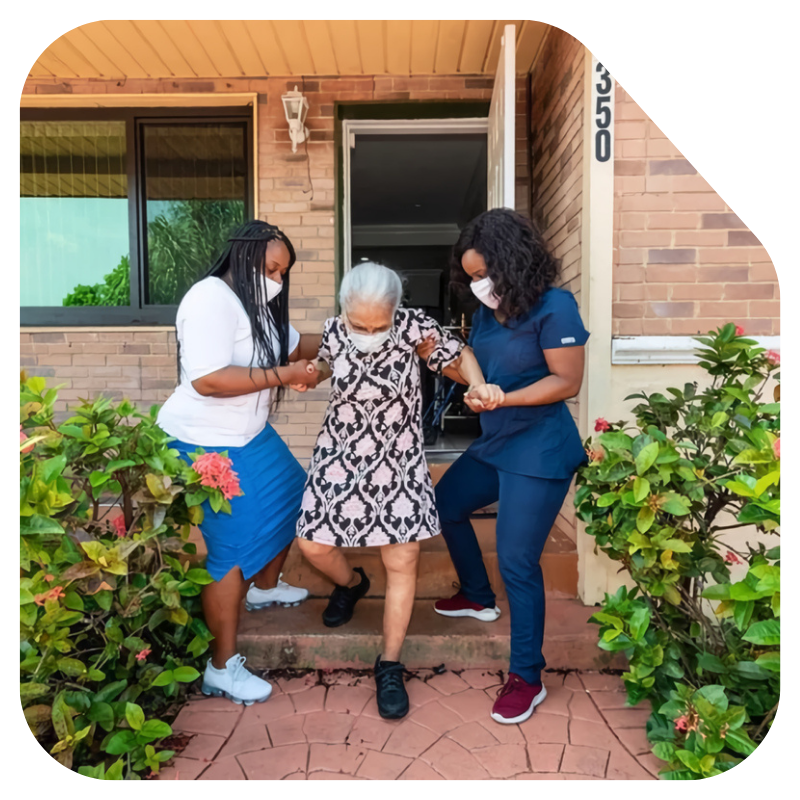 Caregivers assisting an elderly woman with mobility support outside her home in Miami-Dade County, FL